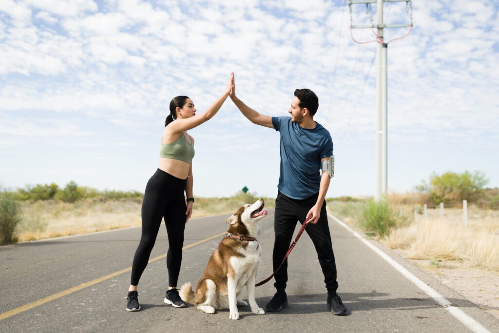 Excited young woman and man making a high five and celebrating finishing a running race with their dog